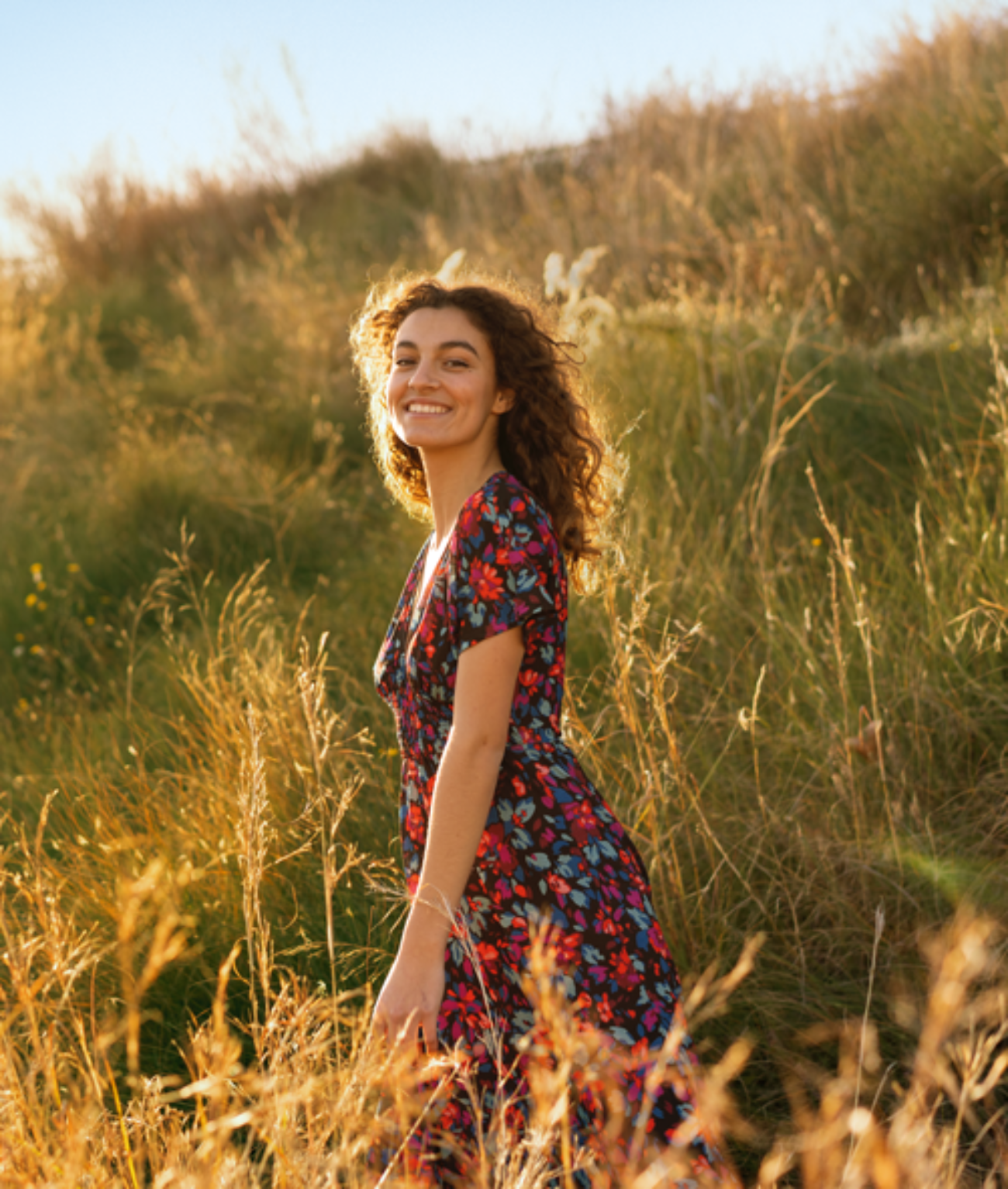 Une femme souriante dans une prairie pendant l'heure dorée.