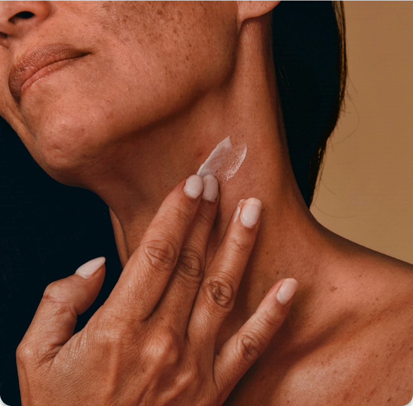 Close-up of a woman's neck as she applies a bit of cream. 