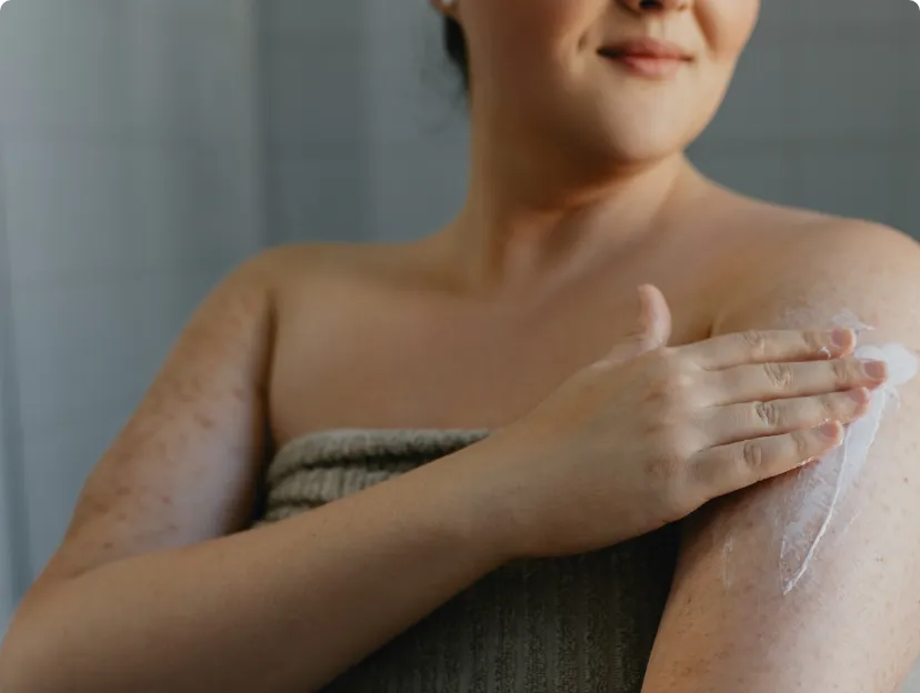 Une femme ayant l'air de bonne humeur s'assoit pour appliquer de la lotion sur ses jambes.